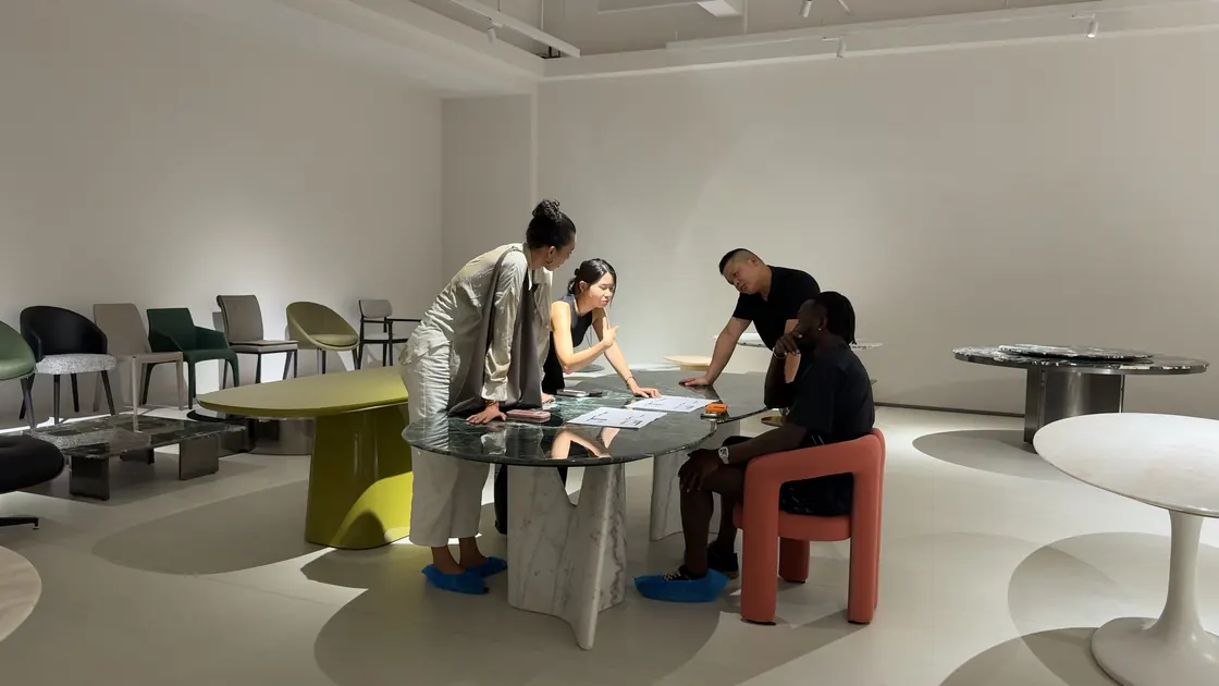 Four adults lean or sit around a round table with printed sheets.