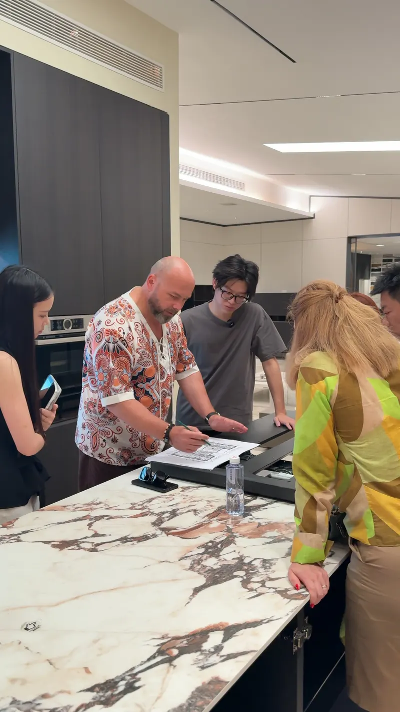 A group gathers around a kitchen counter as one person points at a printed floor plan.