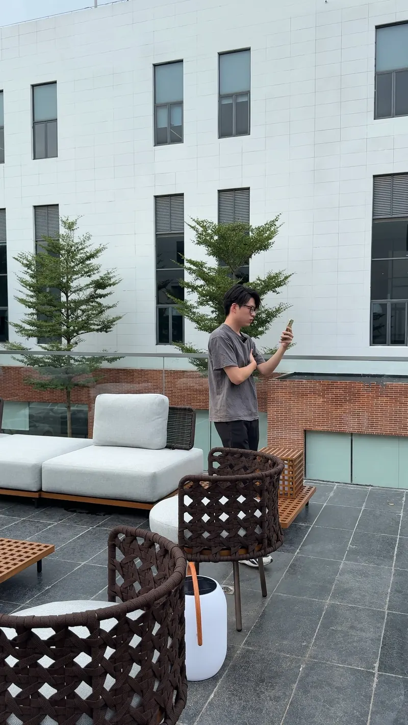 A person holds a phone with its screen facing away from the camera beside outdoor sofa and chair displays.