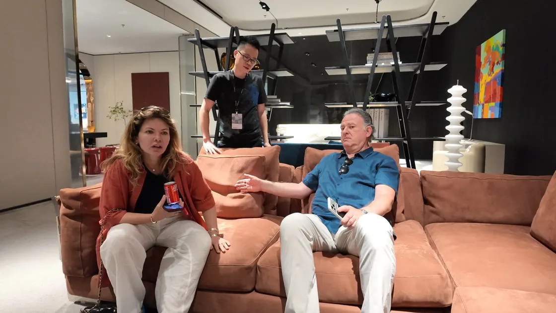Two people sit on a large sofa while another stands behind it.
