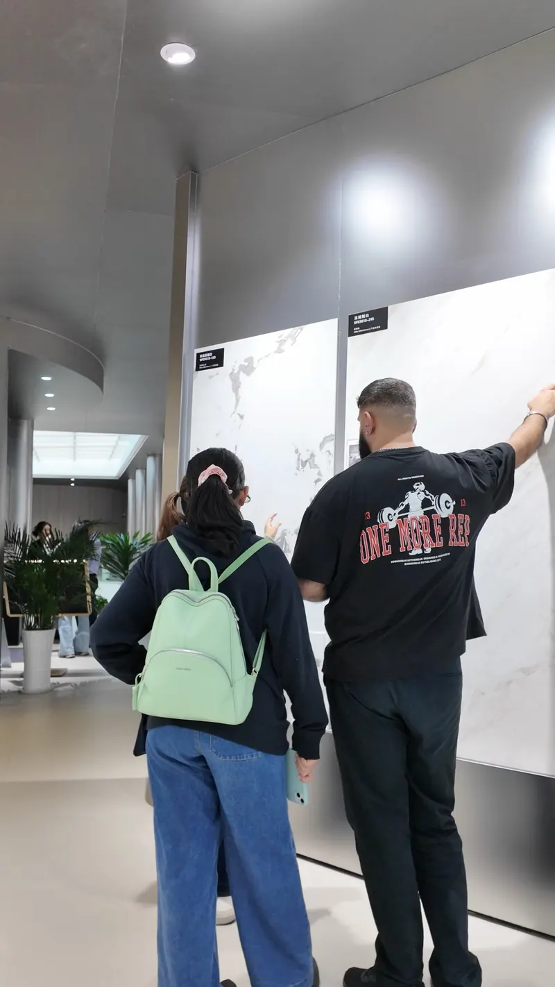 Two people seen from behind touch and point toward large pale veined wall-surface panels.