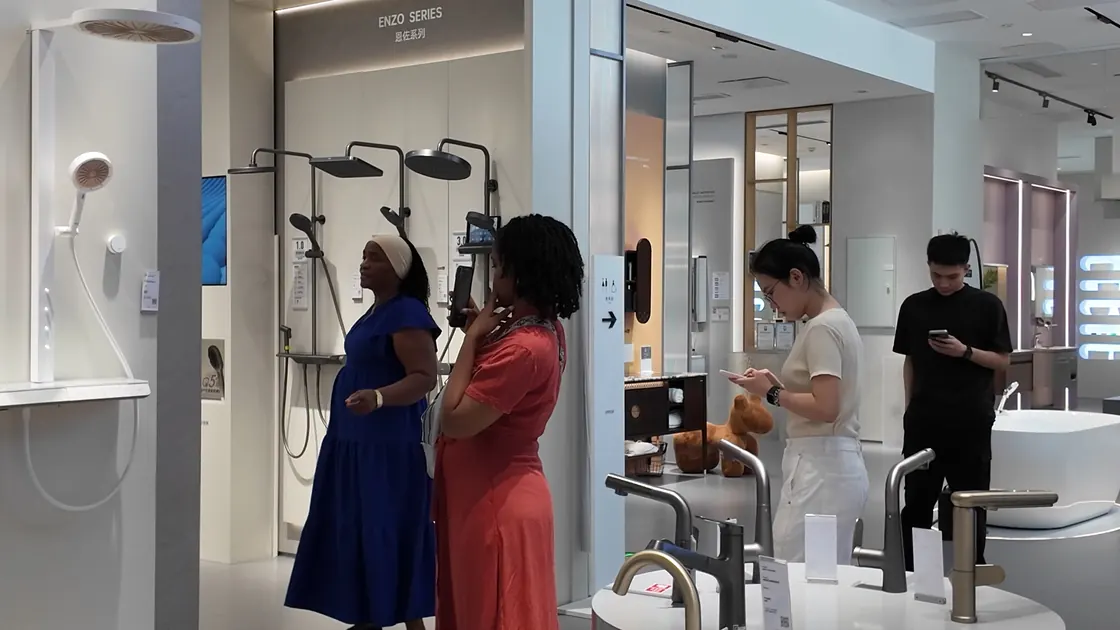 Four people stand among shower fittings and basin displays in a showroom.