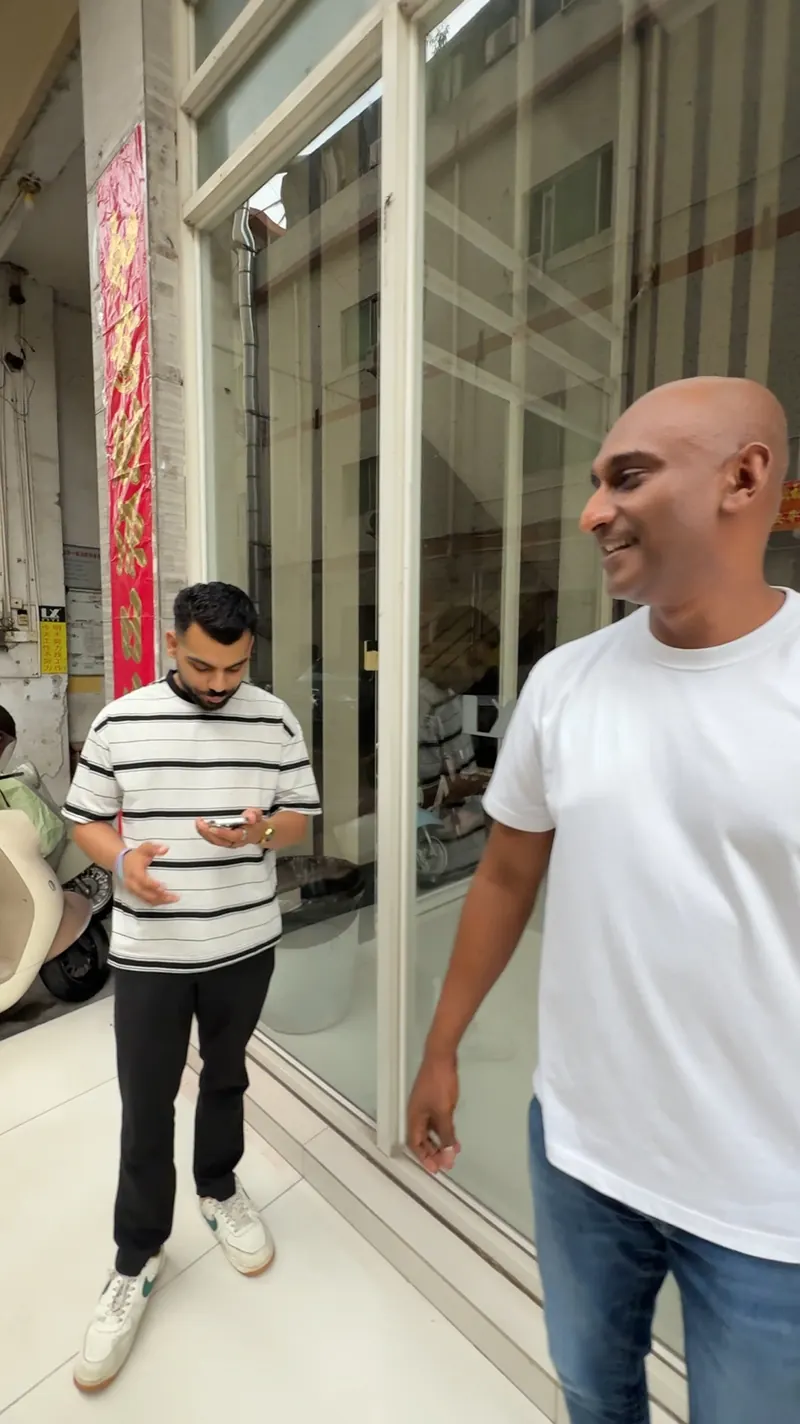 Two adults pause beside a glass showroom entrance; one holds a phone.
