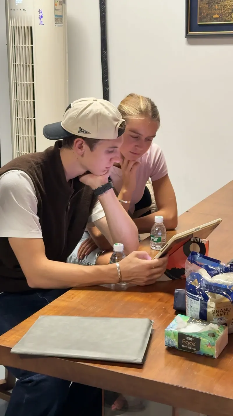Two people lean toward the same tablet at a table.